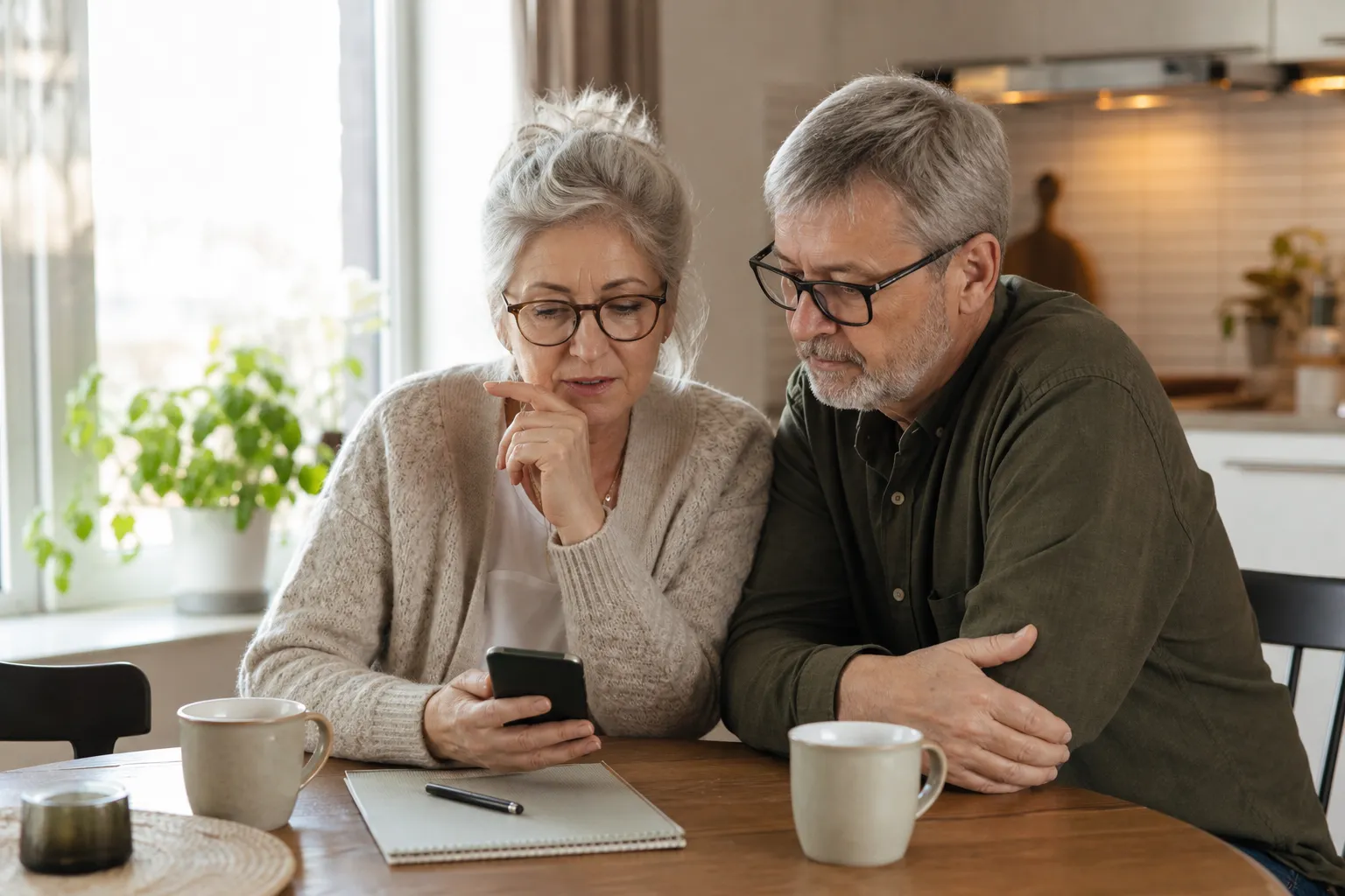 Pensionär jämför billiga mobilabonnemang vid köksbordet med kaffekopp